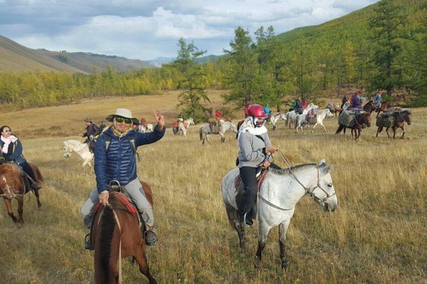 A group of people riding horses in a grassy field with trees in the background. 3