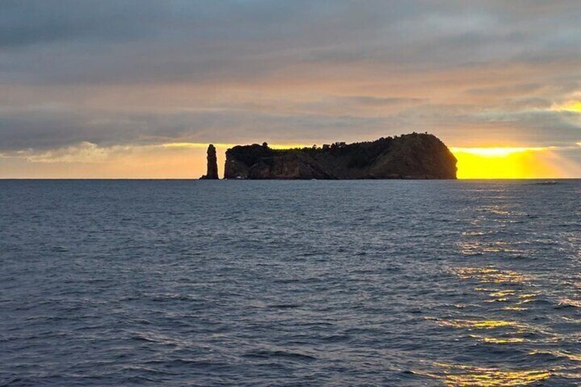 A sunset over the ocean with a rocky island and a lighthouse. 1