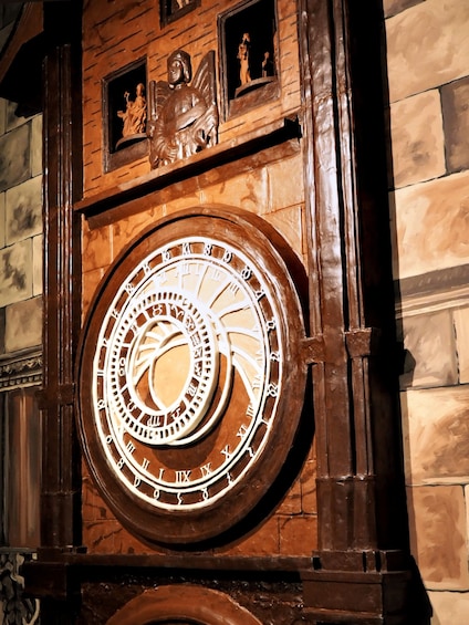 A large, ornate clock with Roman numerals and a circular design, mounted on a brick wall with decorative carvings. 5