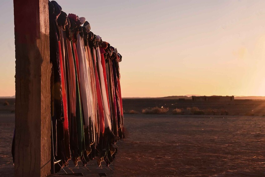 A row of colorful fabrics hanging on a wooden structure in a desert landscape at sunset. 2