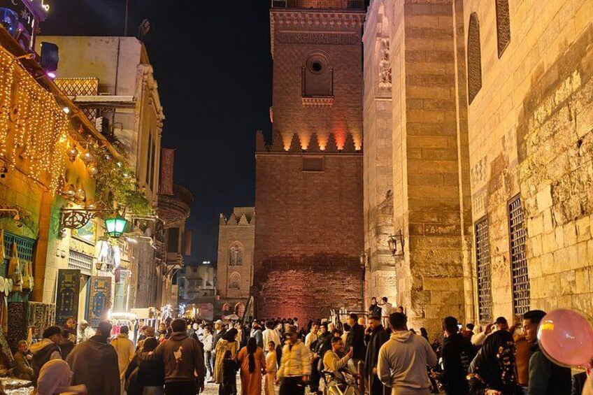 A crowded street at night with illuminated buildings and a prominent tower. 4