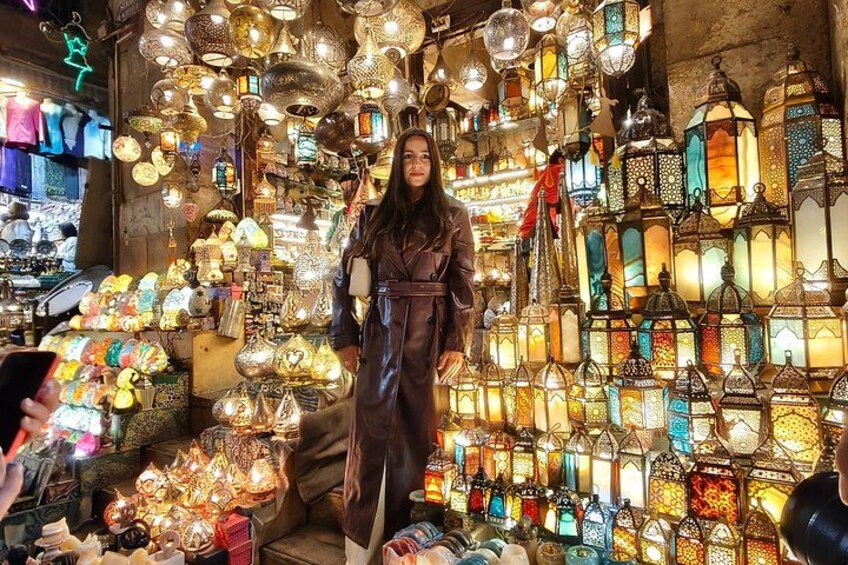 A person standing in a market with various colorful lanterns and lights. 2
