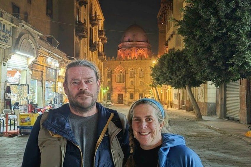 A couple standing on a cobblestone street with a historic building and a dome in the background. 3