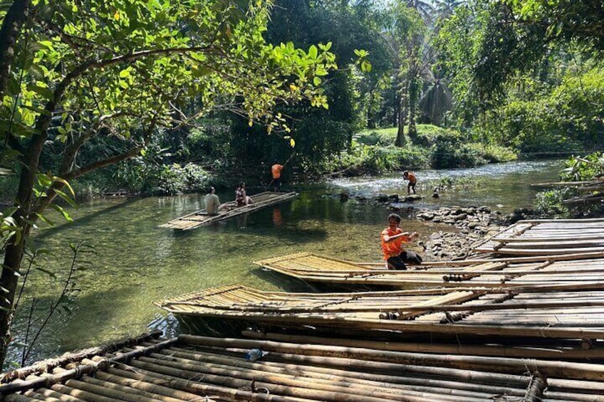 Een rivier met bamboevlotten, een persoon in oranje, en een bebost gebied. 5