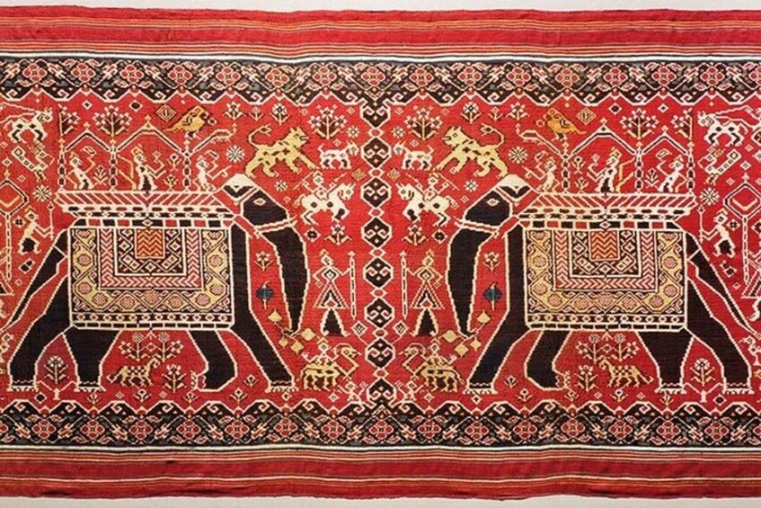 A detailed textile with symmetrical patterns, featuring figures on elephants and geometric designs. 3