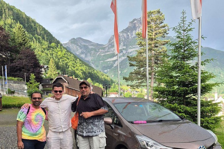 Three people standing in front of a car with a mountainous landscape in the background. 5