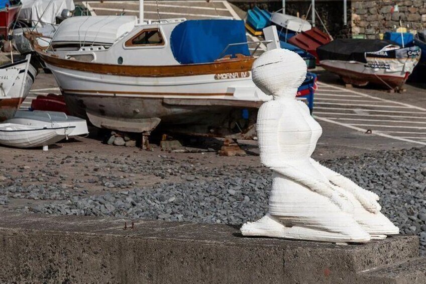 A sculpture of a seated figure on a concrete platform with boats in the background. 4
