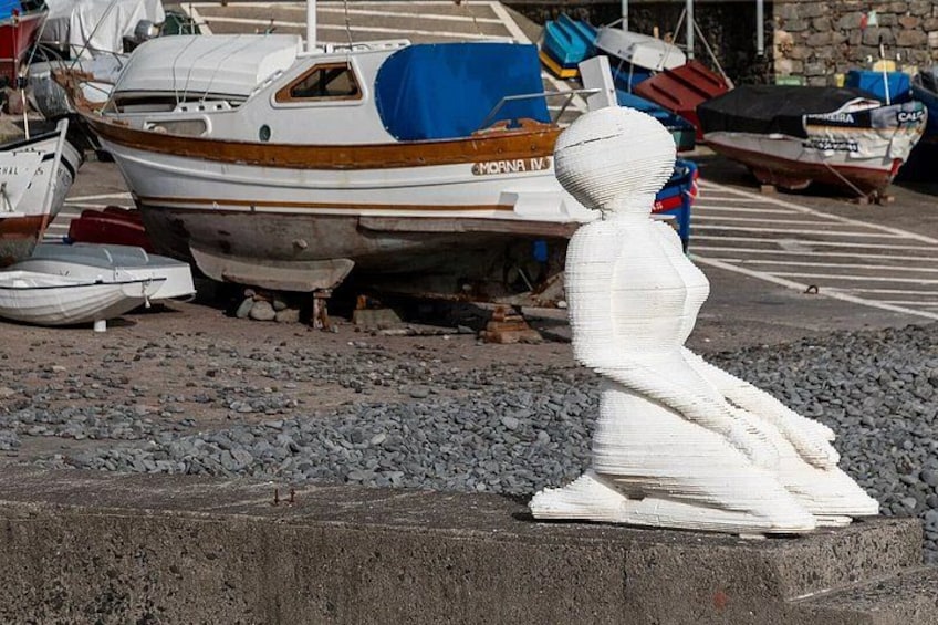 A sculpture of a seated figure, a boat named 'MORNA 1' in the background, and a rocky shoreline. 4