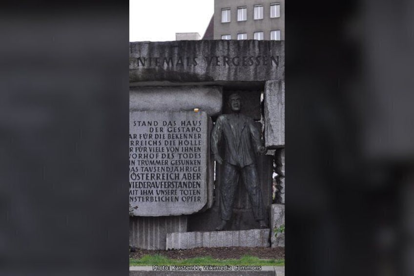 A statue with a plaque, a building in the background, and a sign with text. 3