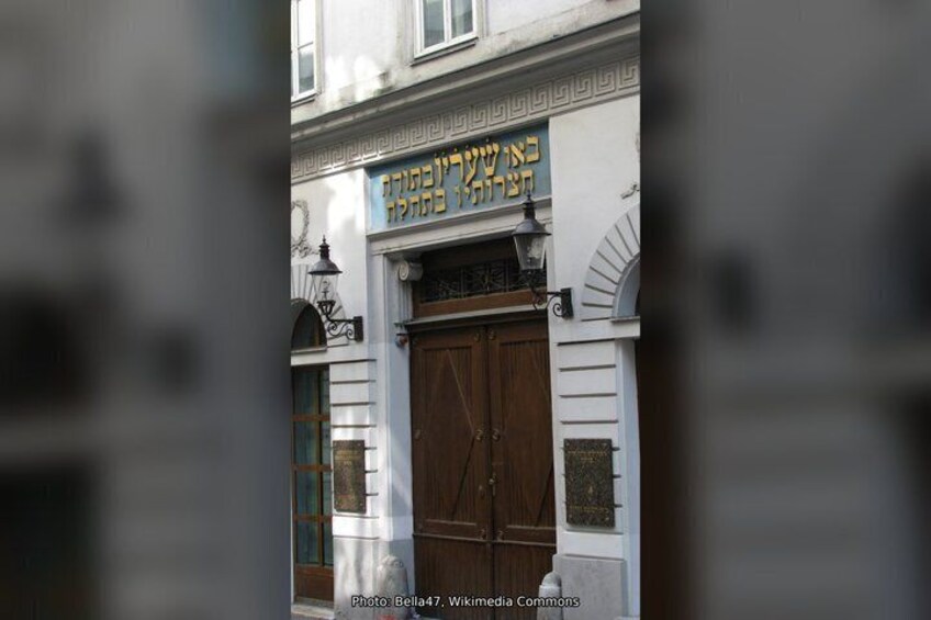 A building with a large wooden door and a sign with Hebrew text. 5