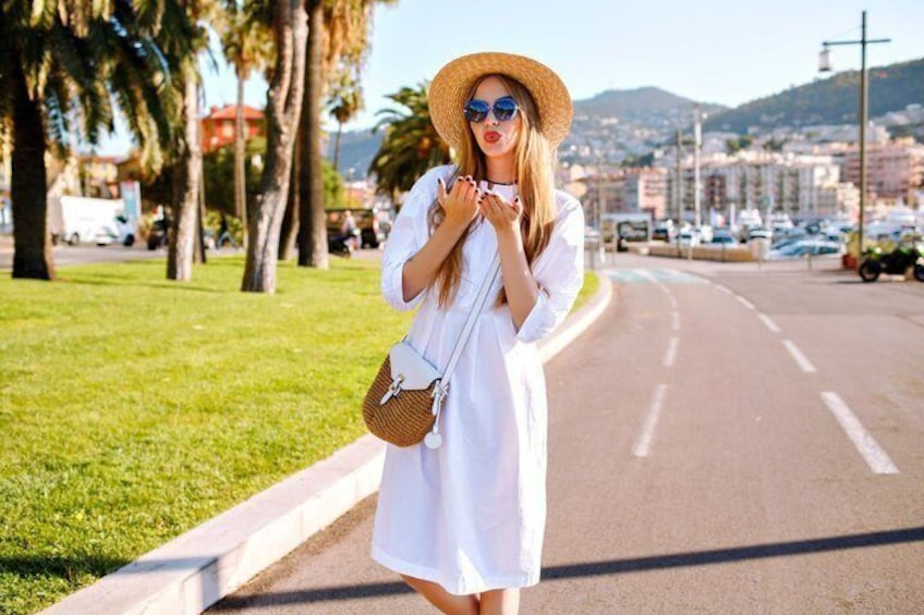 A person in a white dress standing on a road with palm trees and a cityscape in the background. 3