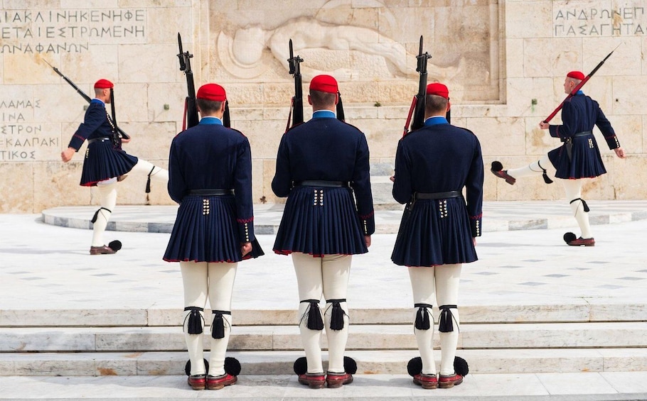 Guards in uniform standing at attention in front of a stone monument. 2