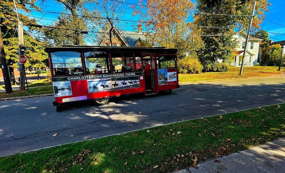 A red trolley with 'CHARLOTTE TOWN SIGHTSEEING TOURS' on its side, parked on a street with autumn leaves and houses in the background. 1