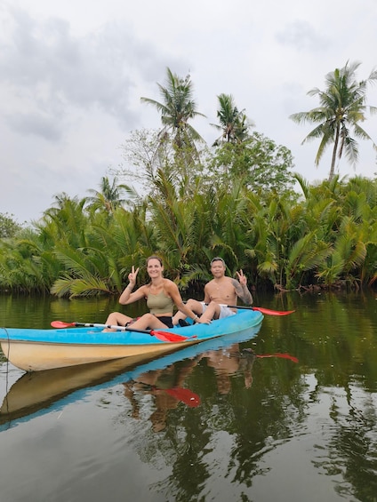 Two people in a blue canoe on a calm river surrounded by lush greenery and tall palm trees. 4