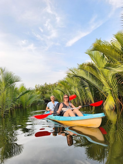 Two people kayaking on a calm river surrounded by lush palm trees. 1