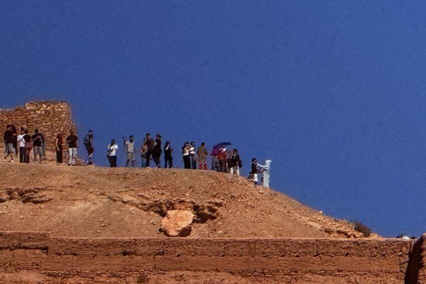 Een groep mensen staat op een rotsachtige heuvel, erboven een helderblauwe lucht. 2
