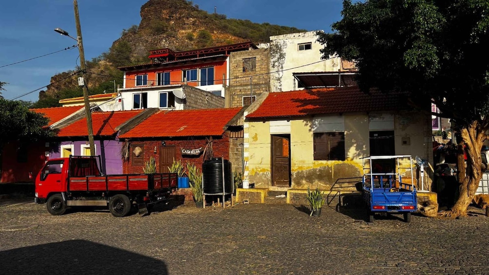 A red truck parked on a cobblestone street, with buildings and a mountain in the background. 5