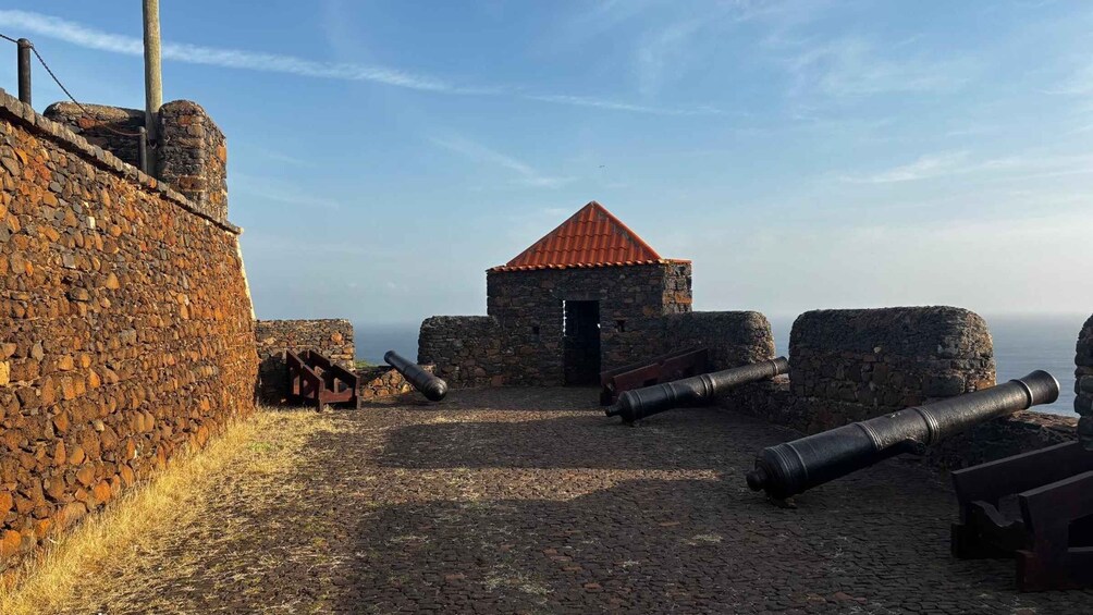 A historic fort with cannons, stone walls, and a small building with a red roof. 3