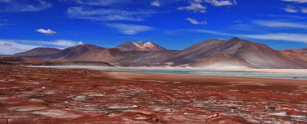 Paisaje desértico con arena rojiza, montañas y una masa de agua. 3