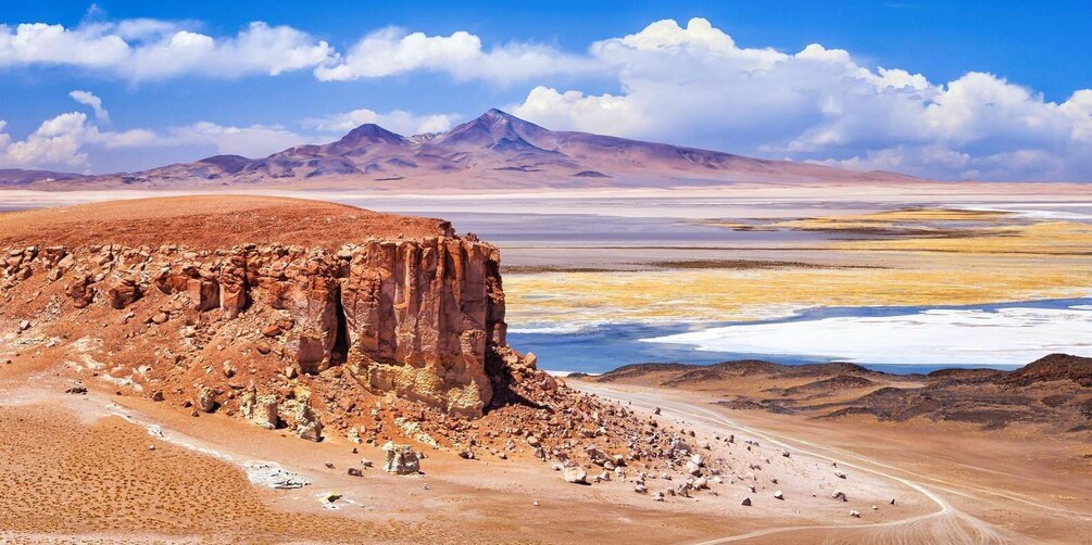 Paisaje desértico con una formación rocosa destacada, una cadena montañosa distante y una planicie salina. 1