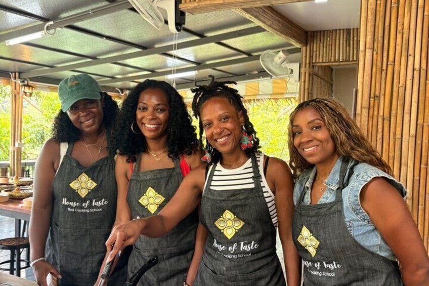 Four people wearing aprons with 'House of Taste' text, standing in a covered outdoor area with bamboo walls. 3
