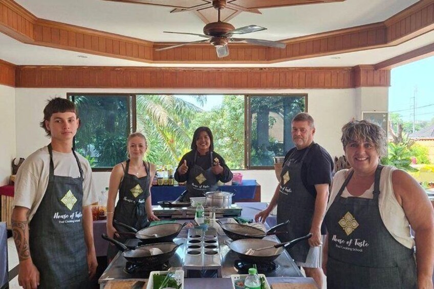 A group of people wearing aprons with 'House of Taste' on them, standing around a kitchen counter with cooking utensils and ingredients. 5