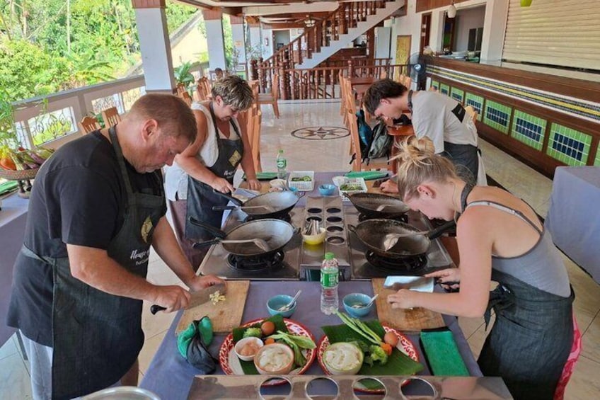 A group of people cooking outdoors at a table with various ingredients and cooking utensils. 4