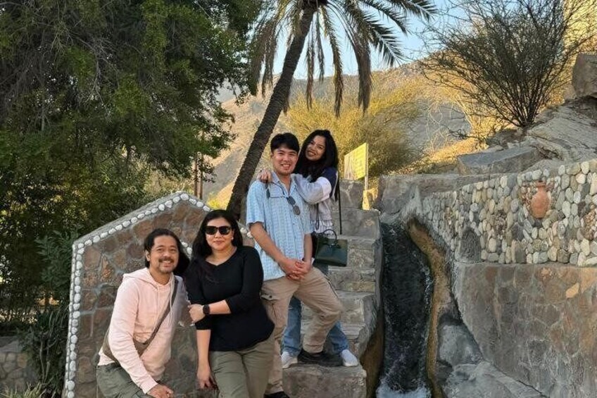 A group of people standing on stone steps with a palm tree and desert vegetation in the background. 5