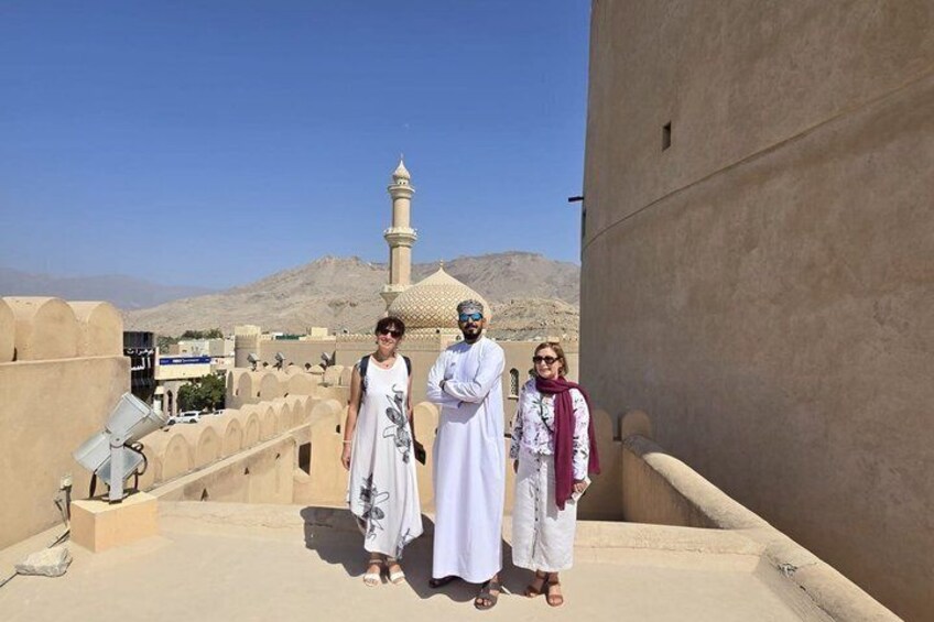 Three people standing on a rooftop with a mosque and mountains in the background. 1