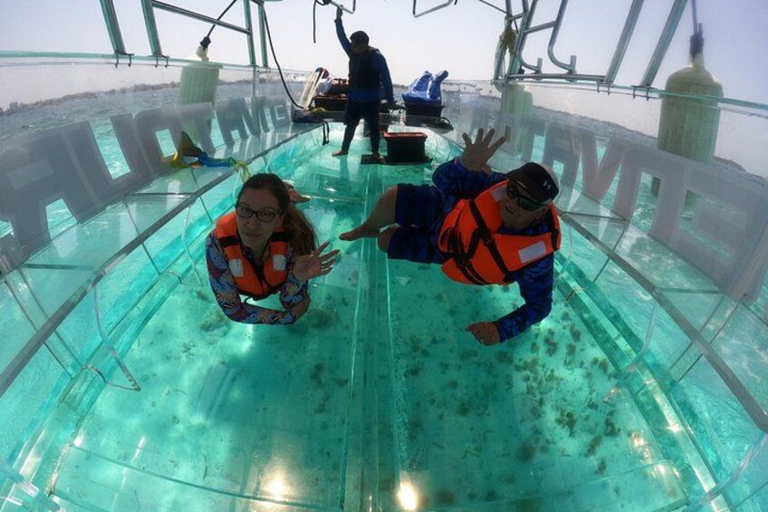 Dos personas en una embarcación con fondo de cristal, con chalecos salvavidas, disfrutando de una vista clara del entorno submarino. 1