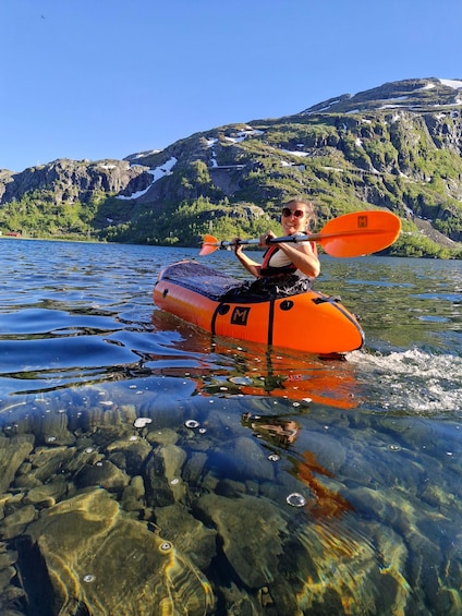 A person kayaking on clear water with a mountainous landscape in the background. 1