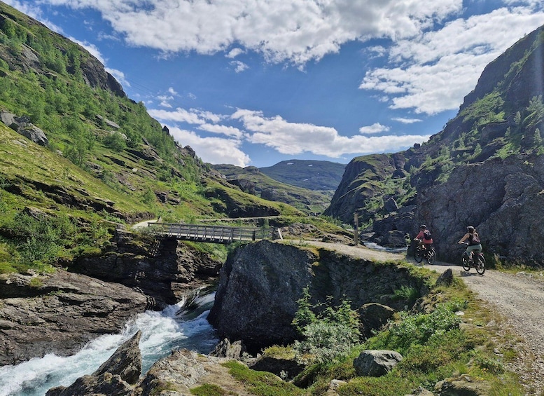 A mountain landscape with a bridge, a river, and cyclists. 4