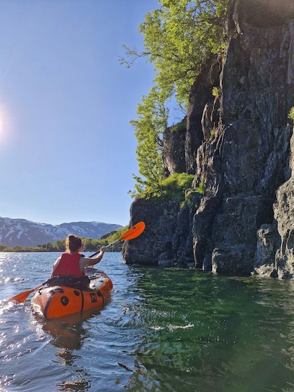 A person kayaking on a calm river, surrounded by rocky cliffs and greenery. 2