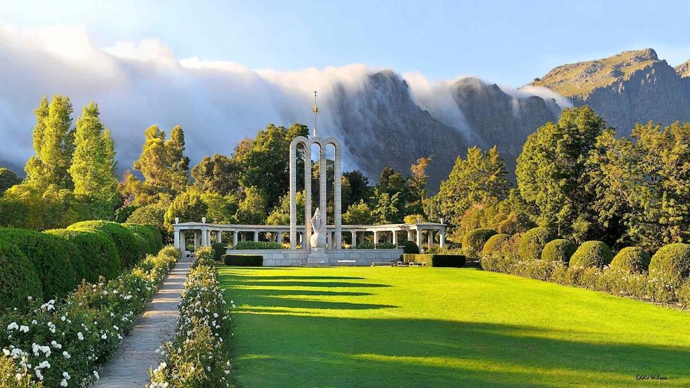 A classical garden with a central statue, manicured lawns, and a mountain backdrop. 3