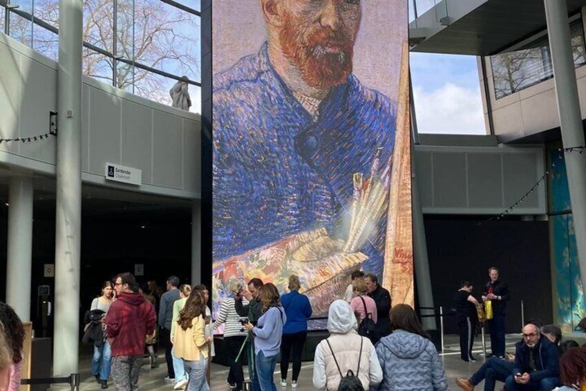 A large mural of a person in a blue jacket, a crowd of people, and a building entrance. 4