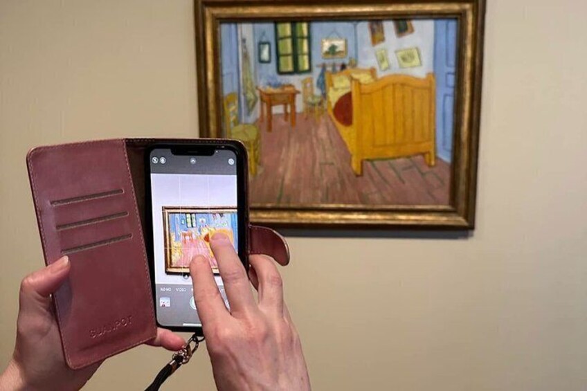 A person holding a smartphone with a leather case, taking a photo of a painting. 5