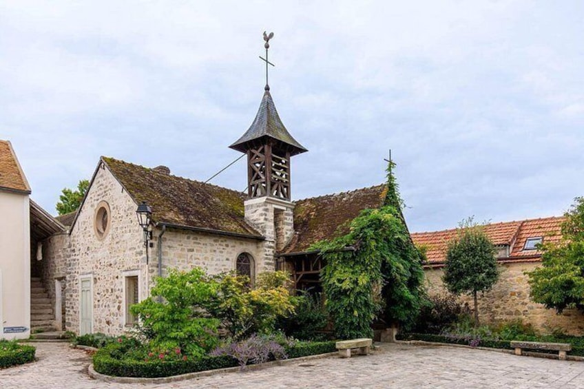 Een stenen kerk met een klokkentoren, omgeven door een geplaveid binnenterrein en weelderige begroeiing. 4