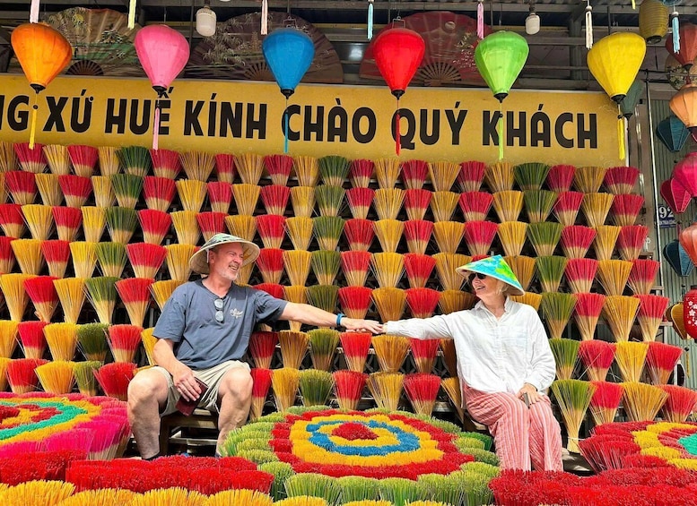 Two people sitting in front of a wall of colorful fans, with a banner above them. 3