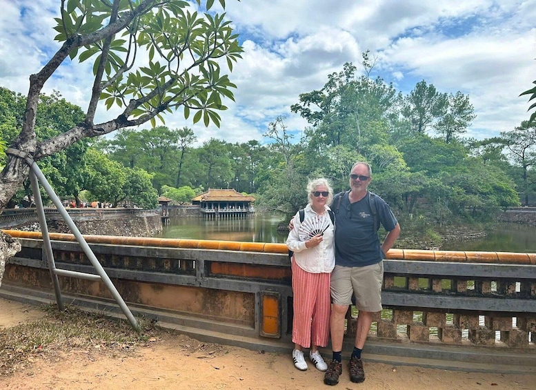 A couple standing by a bridge with a traditional building in the background. 2