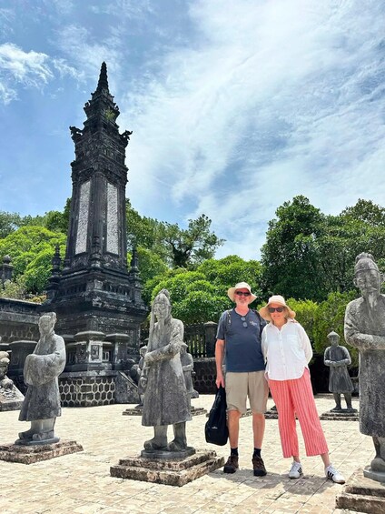 A couple standing in front of a stone monument with intricate carvings, surrounded by similar stone statues and lush greenery. 5