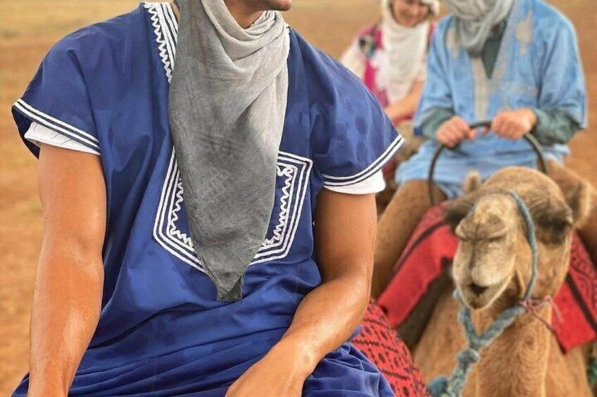 A person in traditional attire sitting on a camel in a desert setting. 4