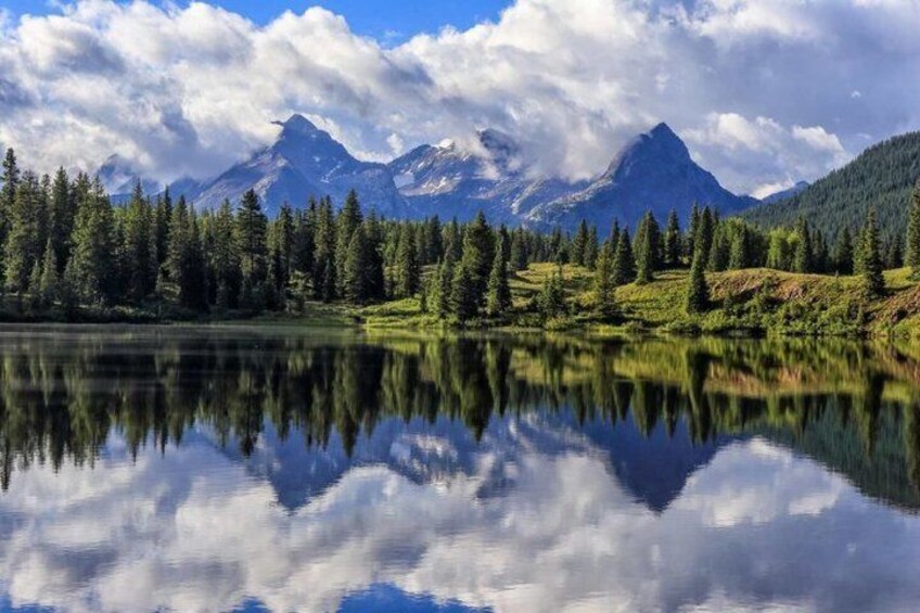 A mountain lake with reflections, surrounded by evergreen trees and snow-capped peaks. 3