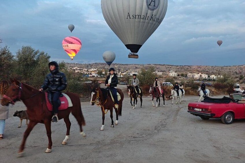 Personas montando a caballo por un sendero de tierra con globos aerostáticos al fondo. 2