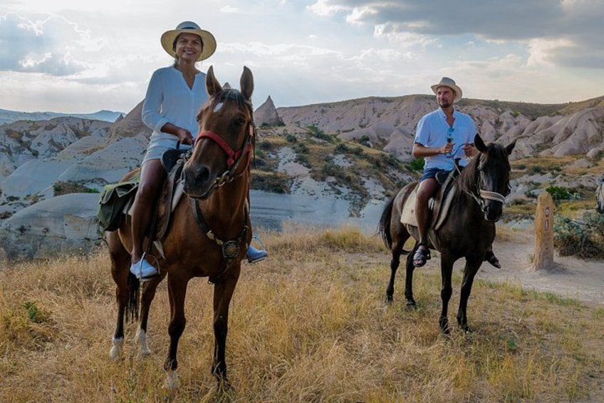 Dos personas montando a caballo en un campo cubierto de hierba, con un paisaje montañoso al fondo. 4