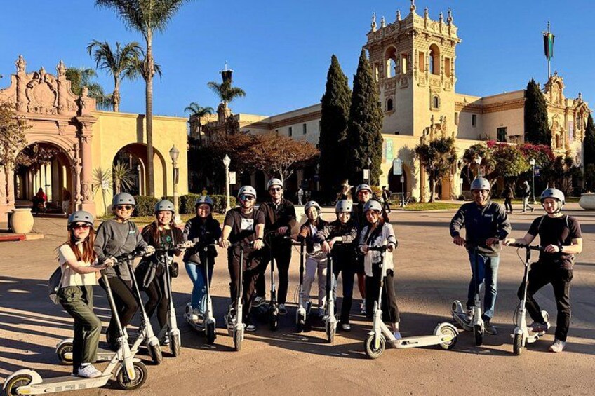 Un grupo de personas en scooters eléctricos en una plaza con un edificio histórico al fondo. 3