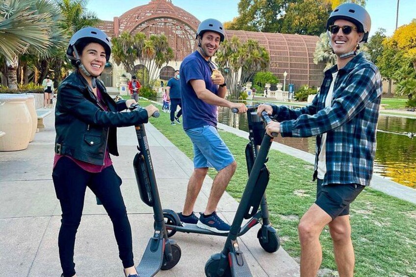 Three people on electric scooters in a park with a lake and palm trees. 2