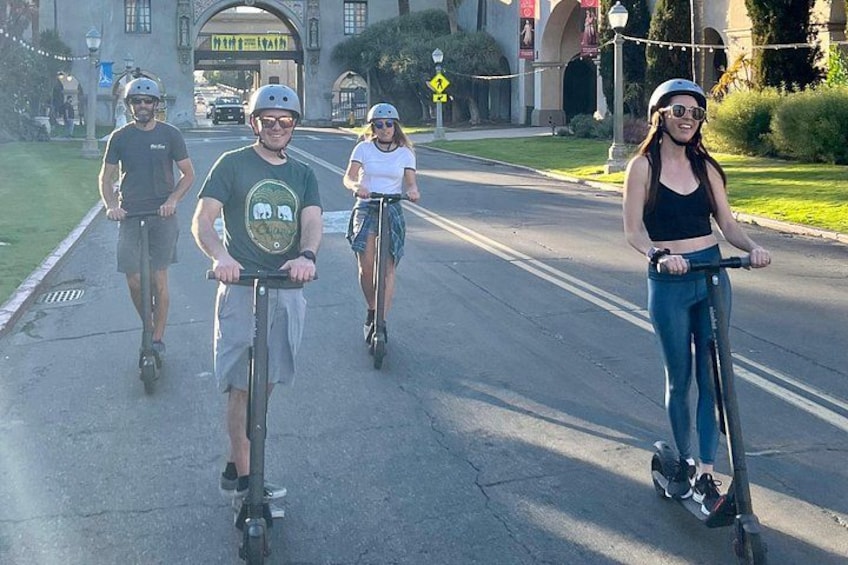 Four people riding scooters on a city street. 4