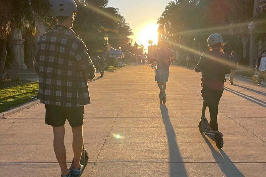 Personas patinando bajo un sol radiante en un parque con palmeras y un atardecer de fondo. 5