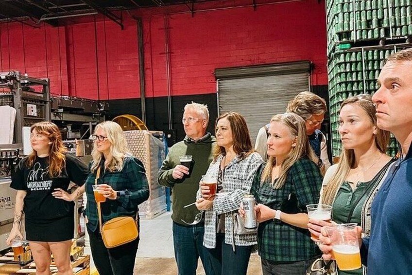 A group of people in an industrial setting with machinery and storage racks. 5
