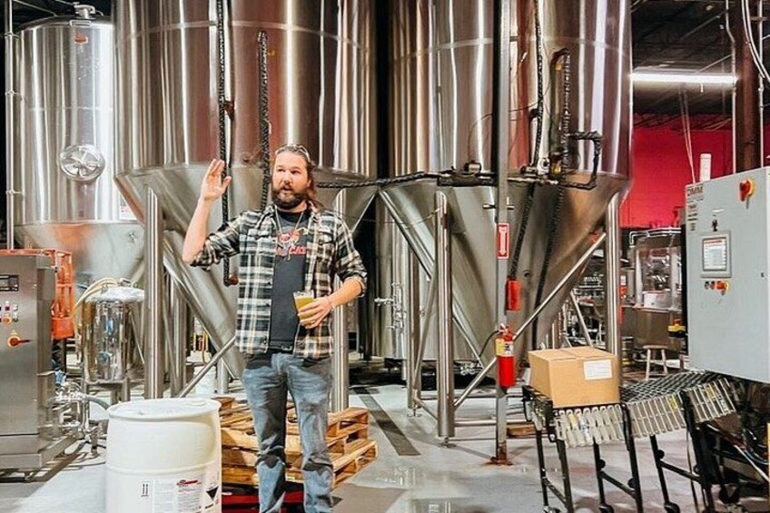 A person standing in a brewery with stainless steel tanks and a conveyor belt. 2